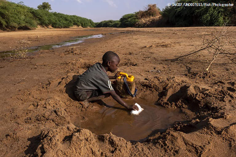 深刻な干ばつにより干上がった川から、わずかな水を集める男の子
